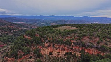 İspanya 'da tepeler ve ağaçlarla kayalık bir manzara görülür. Ön planda, uzak dağlar bulutlu bir gökyüzünün altında belirirken uçurumun kenarları görülüyor. Doğa çevreyi yeşilliklerle dolduruyor..