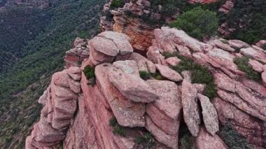 İspanya 'da büyük kaya oluşumları yeşil ağaçların üzerinde yükselir. Sahne, gündüz vakti bir yamaçta taşların çeşitli boyutlarda olduğu kayalık bir alanı gösteriyor..