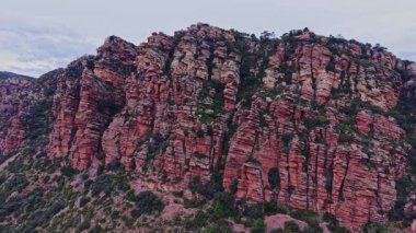 Ziyaretçiler İspanya 'daki çarpıcı kızıl kaya oluşumlarına hayranlar. Sahnede yüksek uçurumlar ve yeşillikler yer alıyor. Bulutlar gökyüzünü kaplıyor ve bu doğal alanı dramatik bir şekilde gösteriyor..