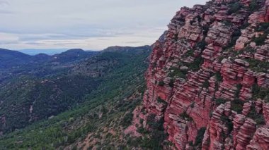 Bir sahnede İspanya 'daki yüksek kayalık dağlar ve yeşil ağaçlar görülüyor. Manzara bulutlu bir gökyüzünün altında kaya ve tepelerin katmanlarını barındırır. Bu, bölgenin doğal güzelliğini yansıtıyor..