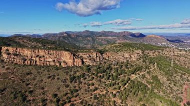 Bir grup insan İspanya 'da bir dağda bir patika boyunca yürür. Gökyüzü bulutlarla mavidir. Manzara arka planda tepeleri ve yeşil ağaçları gösteriyor..