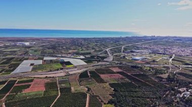 İspanya 'da açık tarlalar, yollar ve deniz manzaralı bir manzara. Ufukta açık gökyüzünün altındaki kentsel bölgelerle yol boyunca tarlalar görülebilir durumda..