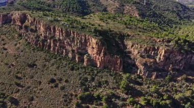 İspanya 'daki kayalıklar ağaçlar ve çalılarla çevrili. Bölge, yeşillik ve engebeli arazi karışımıyla doğal güzellikleri sergiliyor. Güneş doğada parlıyor..