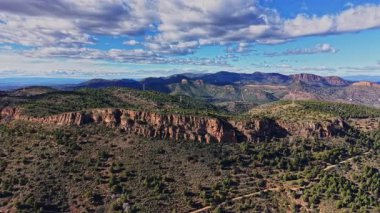 İspanya 'daki kayalık tepelerin ve yeşil ağaçların yüksek manzarası. Sahne, arka planda dağları ve mavi gökyüzünde bulutları gösteriyor. Doğa etrafta hiç insan yokken sergileniyor..