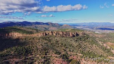 Bu sahnede İspanya 'da mavi bir gökyüzünün altında kayan tepeler ve üzüm bağları gösteriliyor. Arazi bazı kuru bölgelerle yeşildir. Dağlar arka planda görünür, doğal bir manzara yaratır..