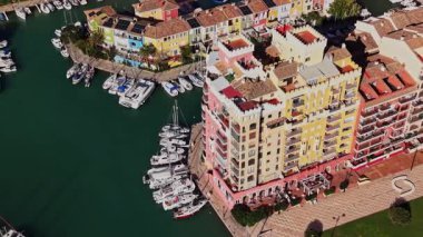 Su binaları parlak renklerle yansıtır. Tekneler rıhtımda dizildi. İnsanlar suyun yanındaki patika boyunca yürüyebilir. Gökyüzü açık güneşli bir gün..