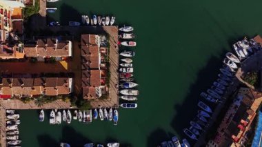 Birçok tekne İspanya 'da binalarla çevrili bir marinada park edilmiştir. Su açık mavi renktedir. Güneşli bir gün. İnsanlar rıhtımda yürüyüp manzaranın tadını çıkarıyor..