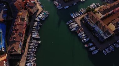 Birçok tekne İspanya 'da bir marinada park edilmiştir. Su sakin ve çevreyi yansıtıyor. Kıyı şeridi boyunca uzanan binalar tipik bir kıyı bölgesini gösteriyor..