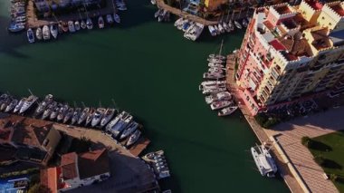 Tekneler İspanya 'da bir marinaya yanaştı. Suyun etrafındaki renkli binalar. Sahne güneşli bir günü gösteriyor. Açık gökyüzü ve yerleşim alanı yakınında sakin sular..