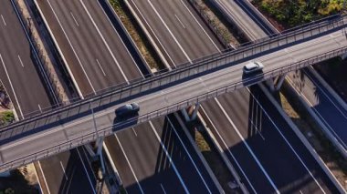 İspanya 'da bir otoyol üst geçidinde iki araba seyahat ediyor. Olay yeri üst geçidin altında birden fazla trafik şeridi gösteriyor. Parlak güneş ışığı, yolda berrak gölgeler yaratır..