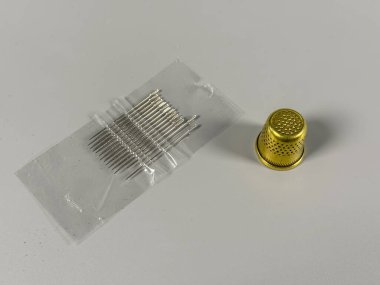 İğneler, sarı bir yüksüğün yanında plastik bir yüzeye konur. Bu ayar dikiş ve zanaat faaliyetlerinde kullanılan araçları gösterir.