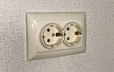 Duvarda iki prizli bir elektrik prizi var. Prizler düz bir yüzeye ayarlanmış ve her delikte iki metal çatal var..