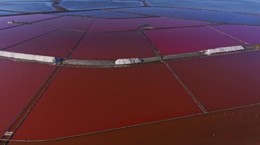 Tuz tarlalarında büyük miktarlarda kırmızı ve beyaz tuz tavaları bulunur. İşçiler tuz toplarken makineler bölgeyi güneşli bir günde bir sonraki hasat için hazırlıyorlar..