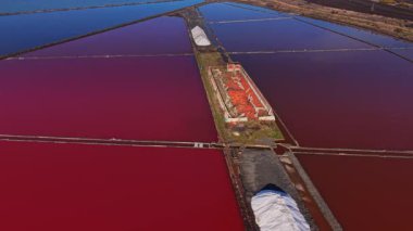 İşçiler çeşitli su renkleriyle dolu büyük havuzlarda tuz topluyor. Tuz yığınları gün ışığında tuz üretim alanı boyunca görülebilir..