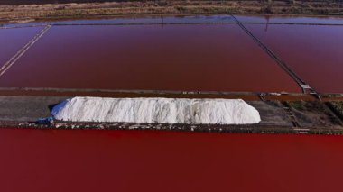 Büyük tuz yığınları kırmızı bir su kütlesinin yanında tuz kaplarında görülür. Bölge gün boyunca tuz toplama ve işleme işçileri ile meşgul..