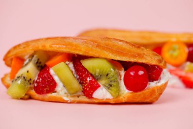 Taze hamur işi kivi, çilek ve kiraz gibi karışık meyvelerle doludur. Tatlı pembe bir zeminde oturuyor, parlak renkler ve dokuları gösteriyor..