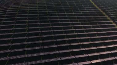 Güneş panelleri geniş bir alana yayılarak enerji üretmek için güneş ışığını yakalar. Bu kurulum yeşil arazi ve çiftliklerle çevrili açık bir alanda yer almaktadır..