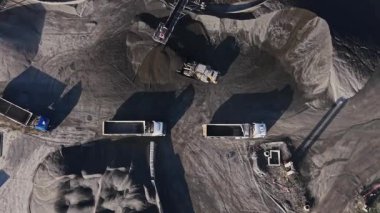 Taş ocağından iki kamyon malzeme yüklüyor. Bölge toprak ve kaya yığınlarıyla dolu. Açık bir günde madencilik ekipmanları yakınlarda çalışır..