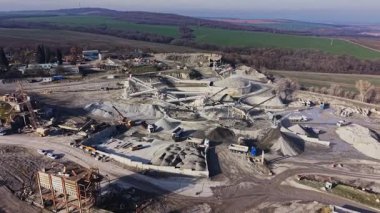 Taş ocağı, taşları ve toprağı hareket ettiren büyük makinelerle aktiftir. İşçiler kamyon nakliye malzemeleri olarak mevcuttur. Çevresindeki manzara tepeleri ve açık gökyüzünü gösteriyor.