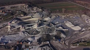 İşçiler büyük bir taş ocağında makine kullanırlar. Taş ve çakıl olay yerinde işlendi. Kamyonlar dizildi ve arka planda yer değiştirme ekipmanları aktif..