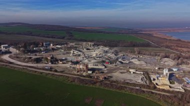 Sahne, çeşitli makinelerin çalıştığı bir taş ocağını gösteriyor. Operasyonlar tepe ve tarlalarla çevrili açık bir alanda gerçekleşiyor. Görünür gökyüzüyle gün aydınlık görünüyor.