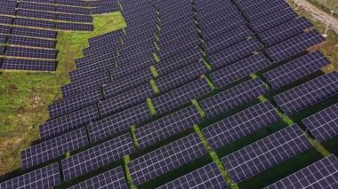 Güneş panelleri büyük bir alanda sıra sıra dizilmiştir. Yer güneşli ve yeşil, yenilenebilir enerji üretimine adanmış bir düzenek sergileniyor..