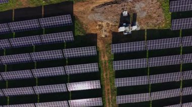 İşçiler yenilenebilir enerji alanına güneş panelleri kuruyorlar. Kurulumda, sürdürülebilir enerji üretimindeki çabaların vurgulandığı, güneş ışığı altında sıralanan sayısız panel sergileniyor.