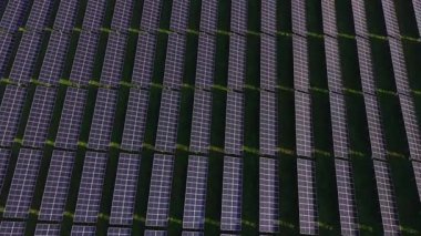 Güneş panellerinin sıraları yeşil bir alan boyunca düzgünce düzenlenmiştir. Ayarlar yukarıda açık gökyüzünü gösteriyor, gündüz saatlerinde kullanılan kurulumu vurguluyor.