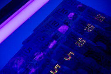 İngiliz sterlin banknotları ultraviyole ışıkla aydınlatılan bir yüzeye yerleştirilir. Işık her notanın güvenlik özelliklerini ve değerlerini açıkça ortaya koyuyor..