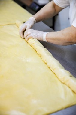 Bir fırıncı mutfakta hamurla çalışır. Kişi hamur işini hazırlarken eldiven ve pürüzsüz hamur işi kullanır. Sahne pişirme sürecini gösteriyor.