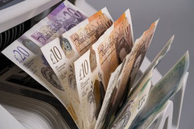 Bir döviz makinesinden çıkan çeşitli banknotların İngiliz sterlin notları gösteriliyor. Olay yeri, paranın mali ortamda işlendiğini gösteriyor..