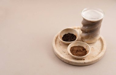 Heykel bardağında minimalist yatay hojicha latte ile kavrulmuş yeşil çay yaprakları ve taş tepside hojicha tozu..