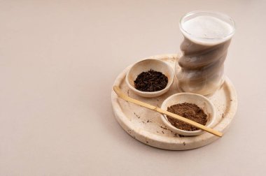 Heykel bardağında minimalist yatay hojicha latte ile kavrulmuş yeşil çay yaprakları ve taş tepside hojicha tozu..