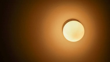 Yuvarlak tavan armatüründen nazik bir ışık parlıyor, sıcak tonlarda odayı yıkıyor. Bu rahatlatıcı atmosfer huzur ve rahatlığı sessiz bir yere davet ediyor..