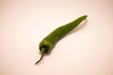 Tek bir taze yeşil biber yalın beyaz arka planda izole bir şekilde yatar..