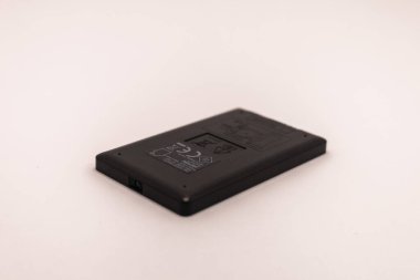 Küçük siyah elektronik cihazın ters tarafı çeşitli düzenleyici işaretler ve ürün bilgileriyle gösterilir. Sade, açık renkli bir yüzeye dayanır..