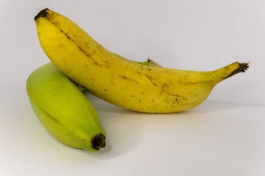 Olgun sarı bir muz ve olgunlaşmamış yeşil bir muz yan yana meyvelerin olgunlaşma sürecini gösteriyor..