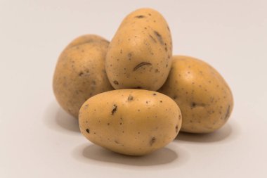 Dört çiğ patates, pişirmeye ya da pişirmeye hazır, beyaz bir yüzeyde sergileniyor..