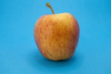 Canlı kırmızı ve sarı bir elma parlak mavi bir arka planda sunulur, görsel cazibe için taze görünümünü vurgular..