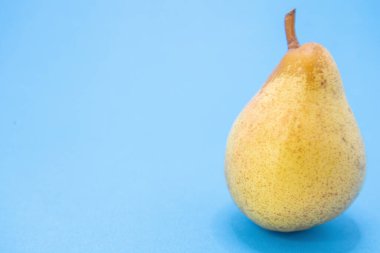 Temiz mavi bir zemin üzerinde, taze ve doğal cazibesini vurgulayan tek bir olgun sarı armut sunulur..