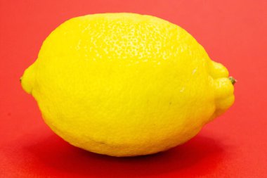 Tek bir parlak sarı limon canlı kırmızı bir arka planda duruyor..
