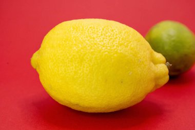 Parlak sarı bir limon, kırmızı arka planda bir limonun önünde oturur..