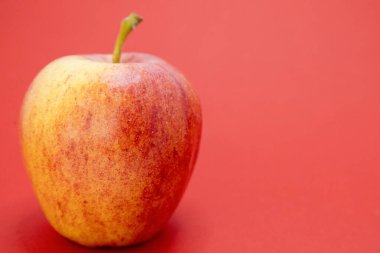 Kırmızı arkaplanda tek bir kırmızı ve sarı elma oturuyor..