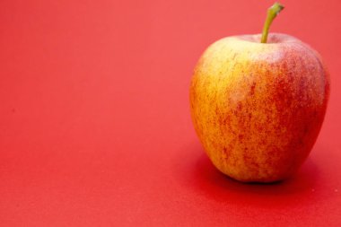 Kırmızı arkaplanda tek bir kırmızı ve sarı elma oturuyor..
