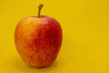 Tek bir kırmızı ve sarı elma parlak sarı bir arka planda oturur..