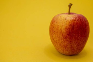 Tek bir kırmızı ve sarı elma parlak sarı bir arka planda oturur..