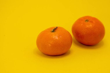 İki parlak turuncu mandalina canlı sarı bir yüzeye oturmuş taze ve renkli bir hayat sunuyor..