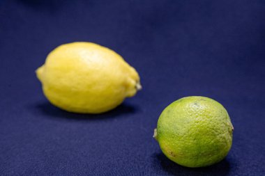 Koyu mavi bir kumaş üzerinde açık sarı bir limon ve yeşil bir limon sunulur..