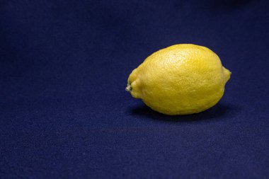 Canlı sarı bir limon derin mavi bir yüzeye uzanır. Sade bir yaşam için taze dokusunu ve parlak tonunu sergiler..