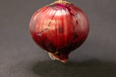 Zengin rengini ve dokusunu gösteren, hafif çatlamış dış derisi olan kırmızı soğan koyu bir arkaplanda fotoğraflanır..